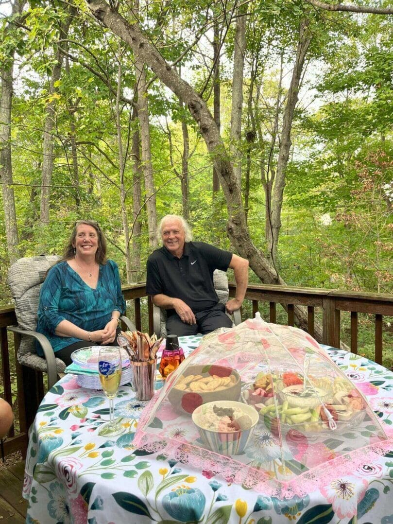 A couple enjoys a meal together on a deck surrounded by trees.