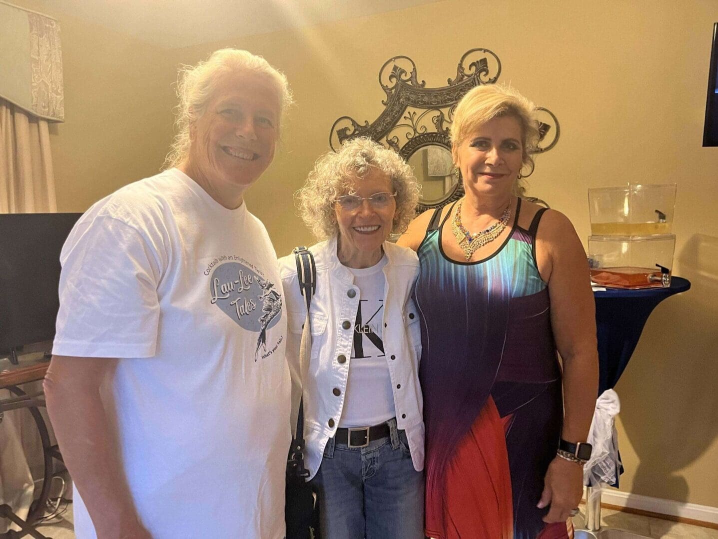 Three people smiling indoors with warm lighting and decorative wall art.