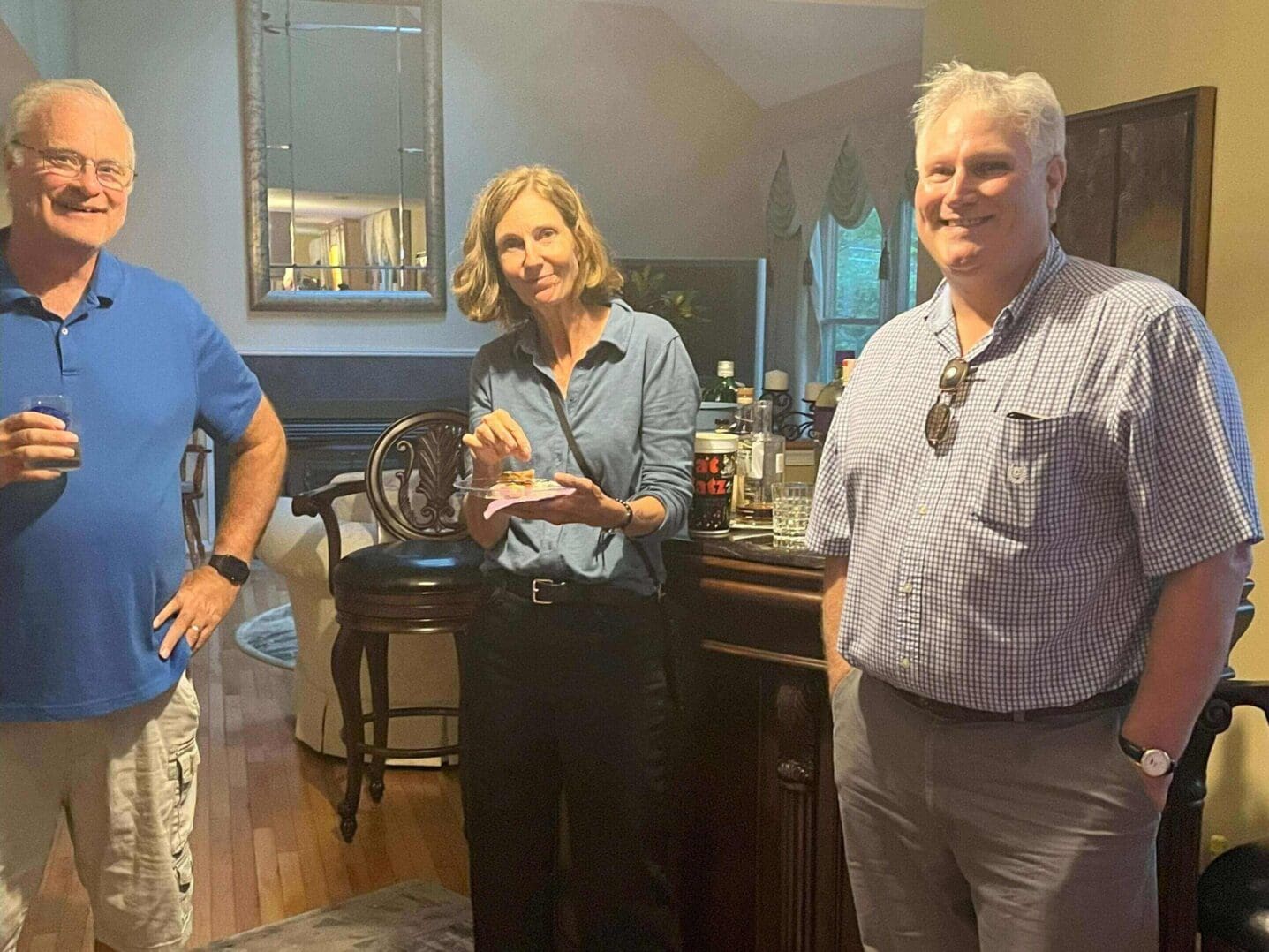 Three adults casually posing indoors, smiling warmly.