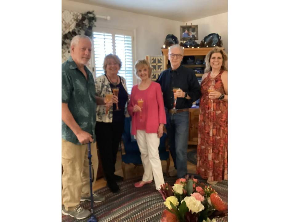 Five people smiling indoors, holding drinks in a cozy living room.