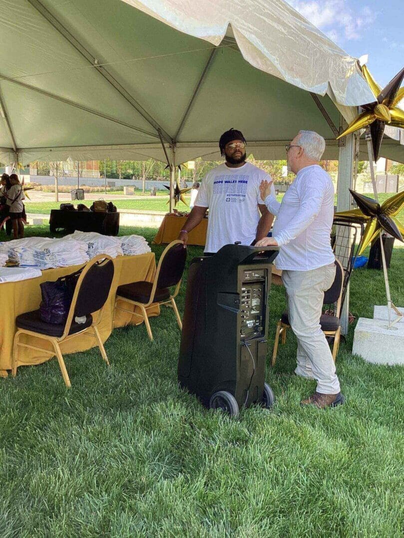 Two men conversing under a tent with a speaker in the foreground.