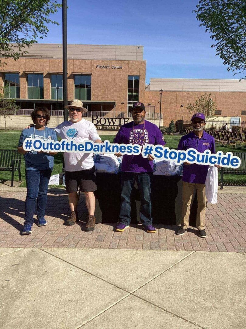 Four people holding a banner promoting suicide prevention outdoors.