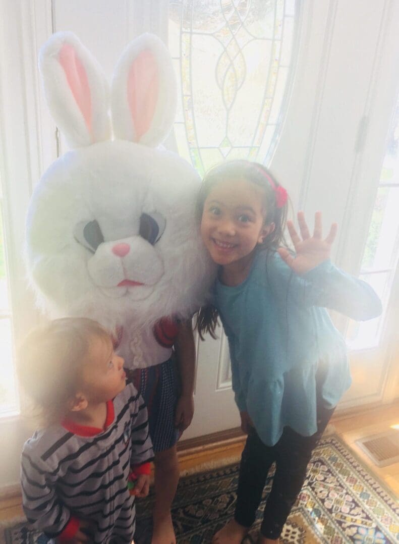 Kids posing with large bunny head indoors.